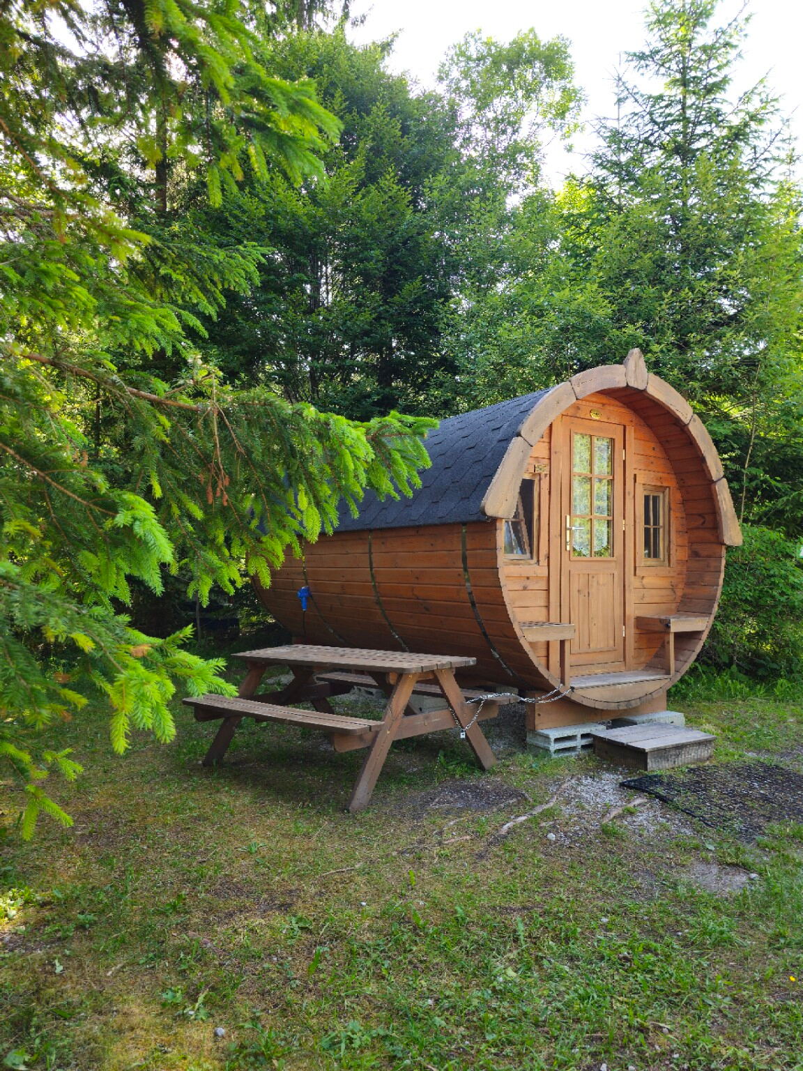 Schlaffass aus Holz zwischen Bäumen auf dem Naturcampingplatz Isarhorn